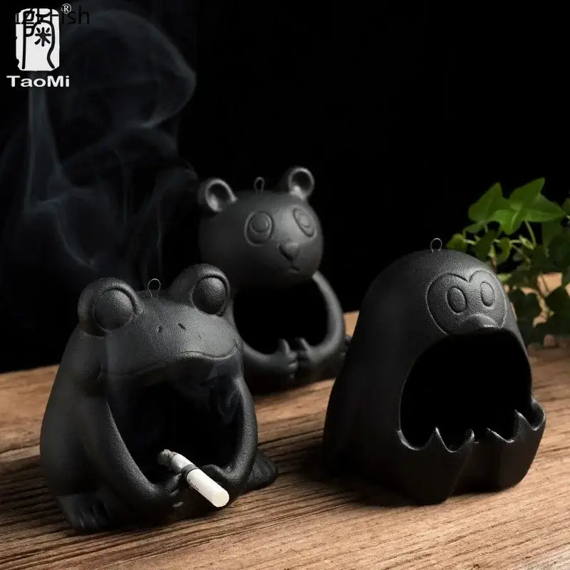 Cute black and gold ceramic ashtray shaped like a cartoon animal frog holding a cigarette with rising smoke for decor