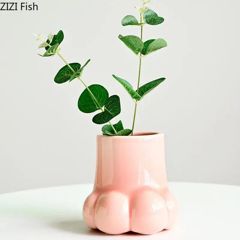 A cute cartoon cat paw ceramic vase in glossy pink holding eucalyptus stems with small white flowers for living room decor