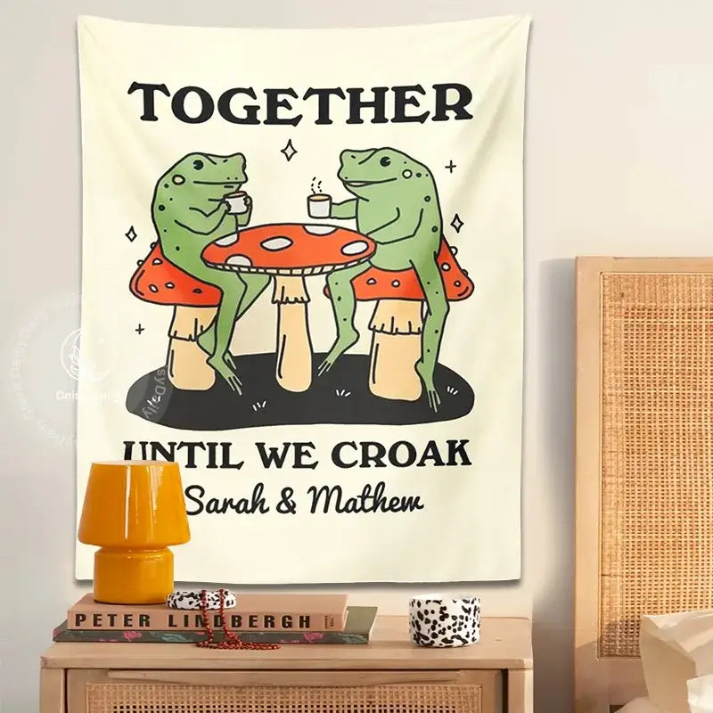 Cream-colored wall tapestry featuring a cute cartoon frog moon with two green frogs at a mushroom table and personalized text