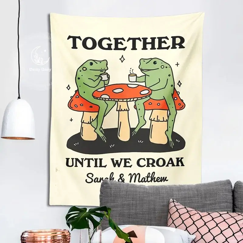 Cream-colored wall tapestry featuring a cute cartoon frog moon design with two green frogs on red mushrooms sipping tea