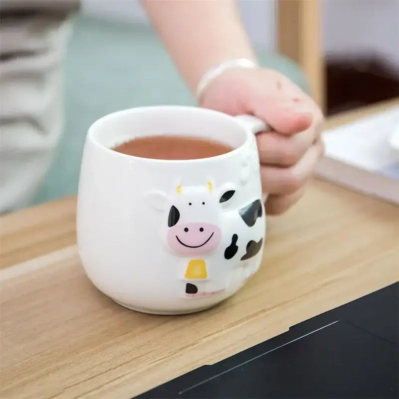 White and black decorbites cow ceramic mug featuring a cheerful cow with yellow horns holding a warm beverage