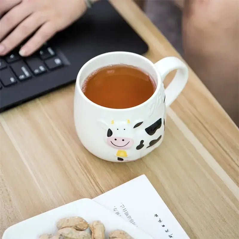 White and black cow ceramic mug by decorbites featuring a smiling cow design filled with amber tea for kitchen use