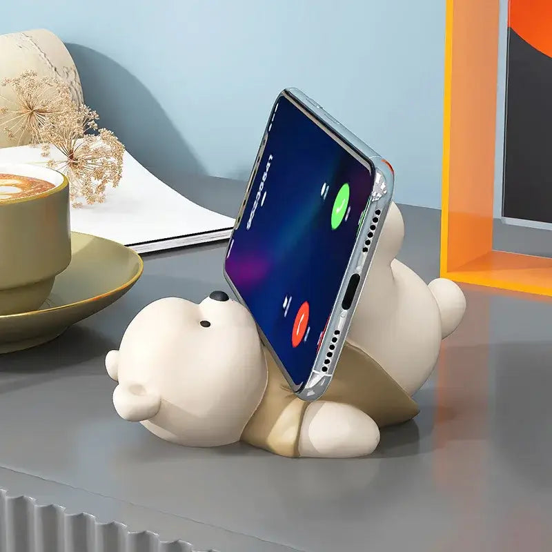 Cream-colored ceramic bear cellphone stand holding a smartphone upright as a cute desktop ornament