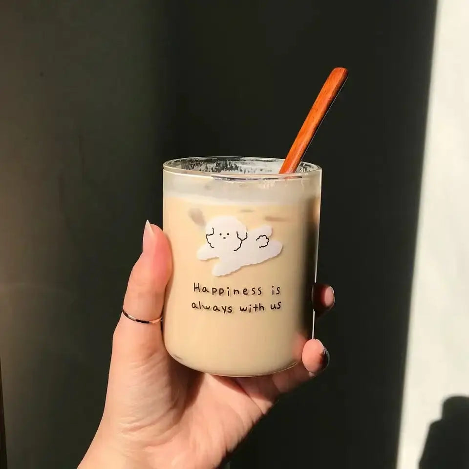A clear glass cup with a white cloud sticker and happiness is always with us text holding an iced beverage