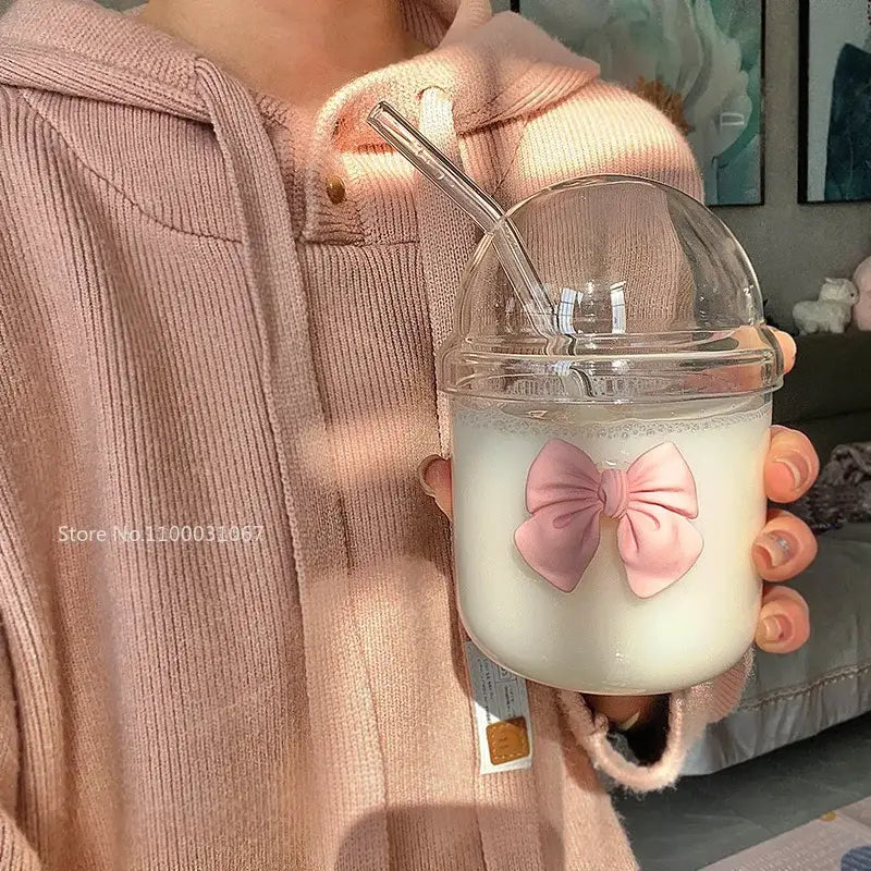 A clear plastic cup with dome lid filled with creamy beverage and decorated with a pink bow tie