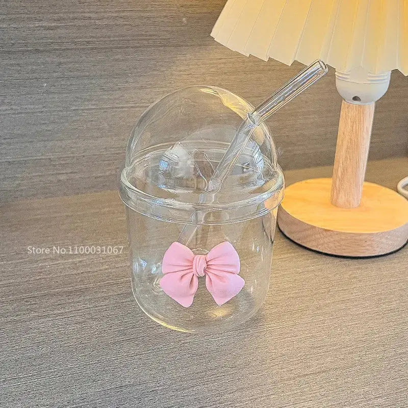 Clear glass cup with dome lid and integrated straw featuring a pink bow tie for kitchen coffee use