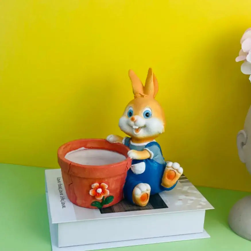 A cheerful orange ceramic bunny rabbit figurine in blue overalls beside a terracotta rabbit flower pot decor