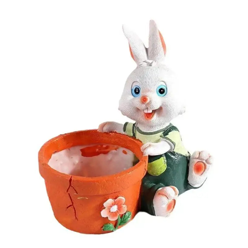 A cheerful white bunny rabbit figurine with blue eyes wearing green overalls sits beside an orange ceramic rabbit flower pot with a pink flower