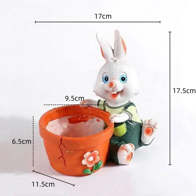 White bunny rabbit figurine with blue eyes in green overalls beside cute orange ceramic rabbit flower pot with pink flower decor