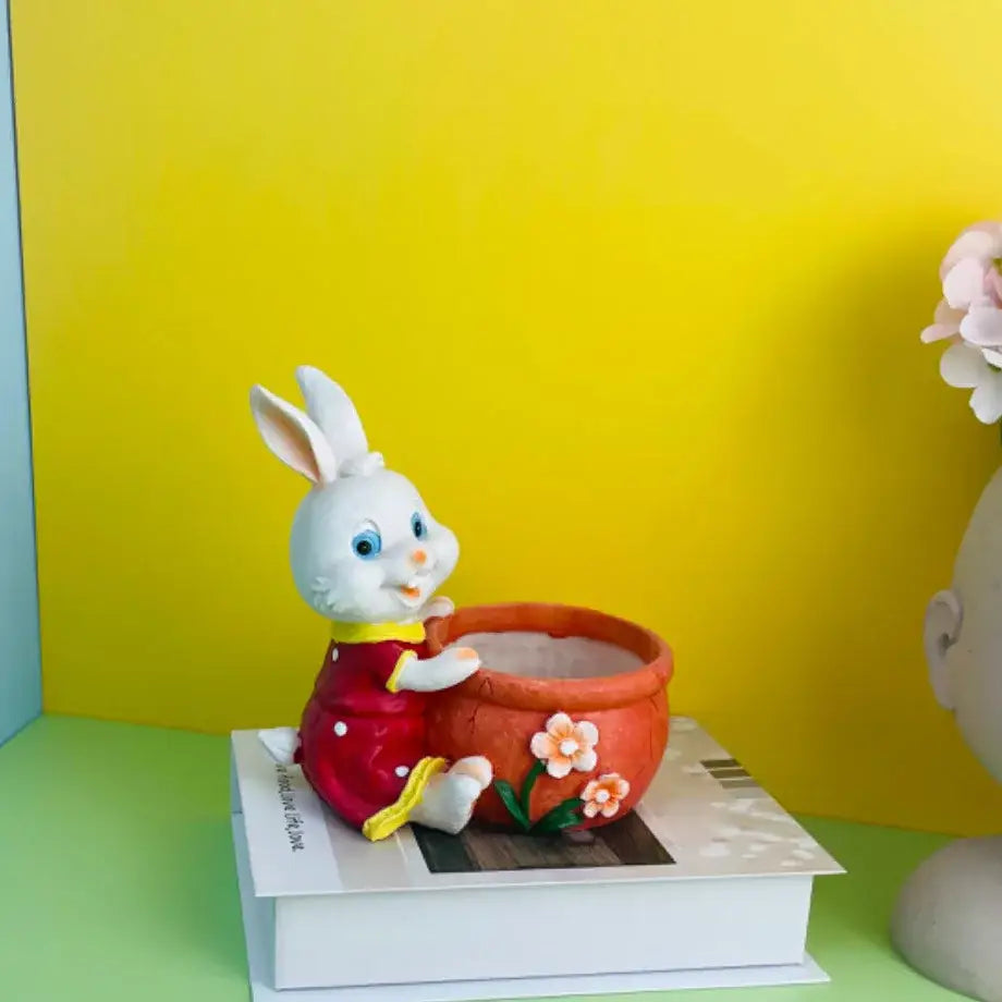 White bunny rabbit flower pot figurine in red dress holding an orange ceramic pot with pink flowers garden decor