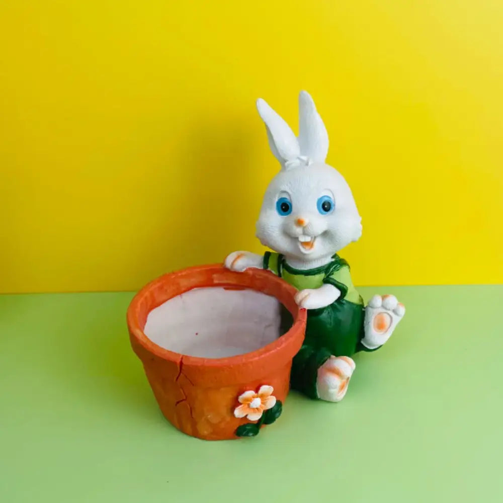 White plastic bunny rabbit figurine in green overalls sitting beside an orange ceramic rabbit flower pot with floral decoration