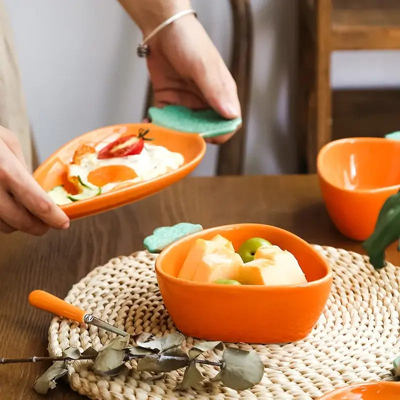 Orange ceramic bowl with green leaf-shaped handle from a cute ceramic tableware set for dining room use