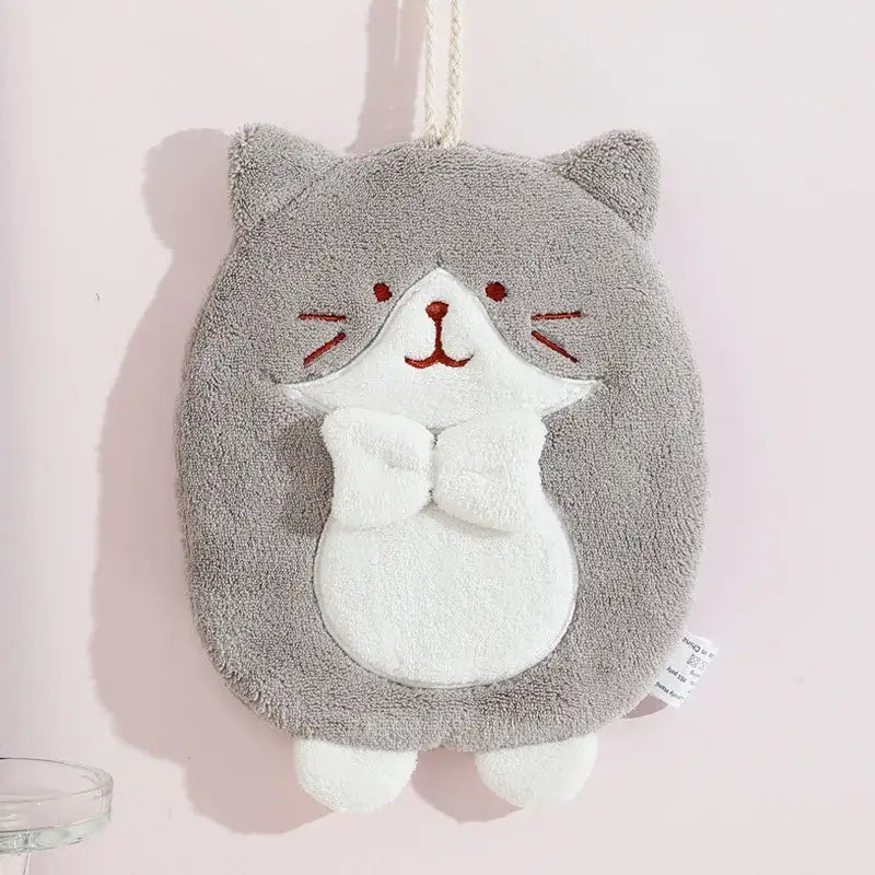Gray plush cat hand towel with white belly and red embroidered face hanging by rope in bathroom plush sponge design