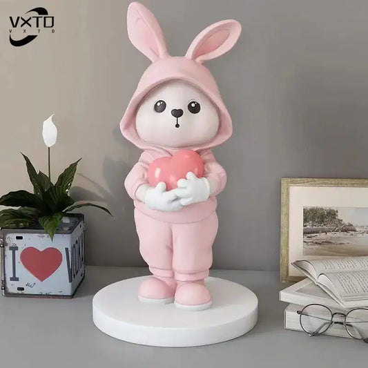 A soft pink resin rabbit desk figurine in a hooded outfit holding a heart for home decor