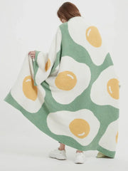A cozy green knitted throw with a cute poached egg pattern featuring white and yellow fried eggs for bedroom decorbites decor