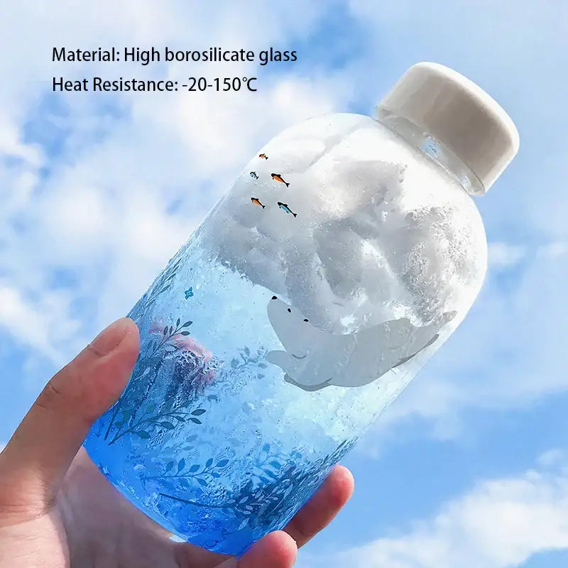Transparent blue glass water bottle with white lid and underwater design featuring fish and smiling whale decorbites blue glass