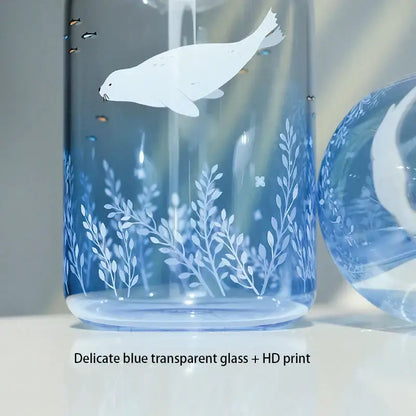A delicate decorbites blue glass water bottle featuring a white seal hd print among aquatic plants and fish