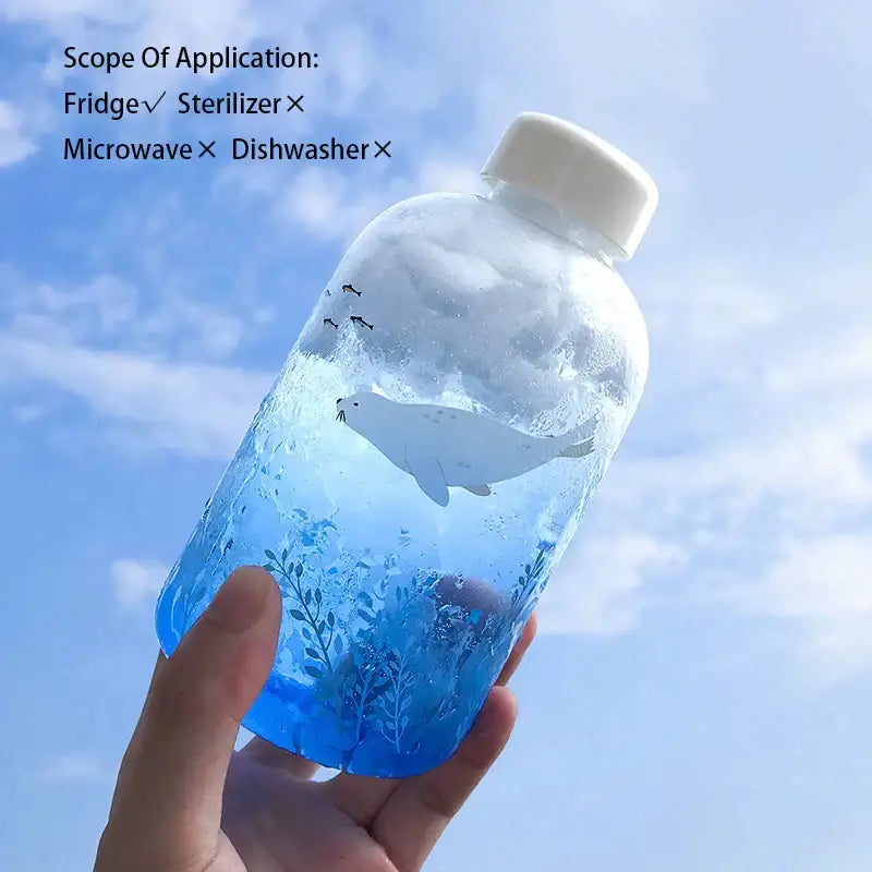 Clear plastic water bottle with white cap featuring illustrated seal in blue liquid and aquatic plants decorbites blue glass water
