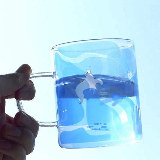 Clear glass coffee mug with handle featuring an illustrated polar bear swimming in blue liquid heat resistant design