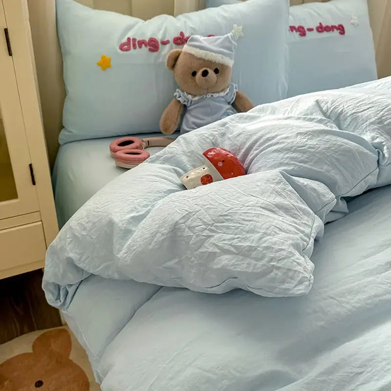 A plush teddy bear in a light blue nightgown and star hat on a soft blue decorbites cartoon embroidery bed set