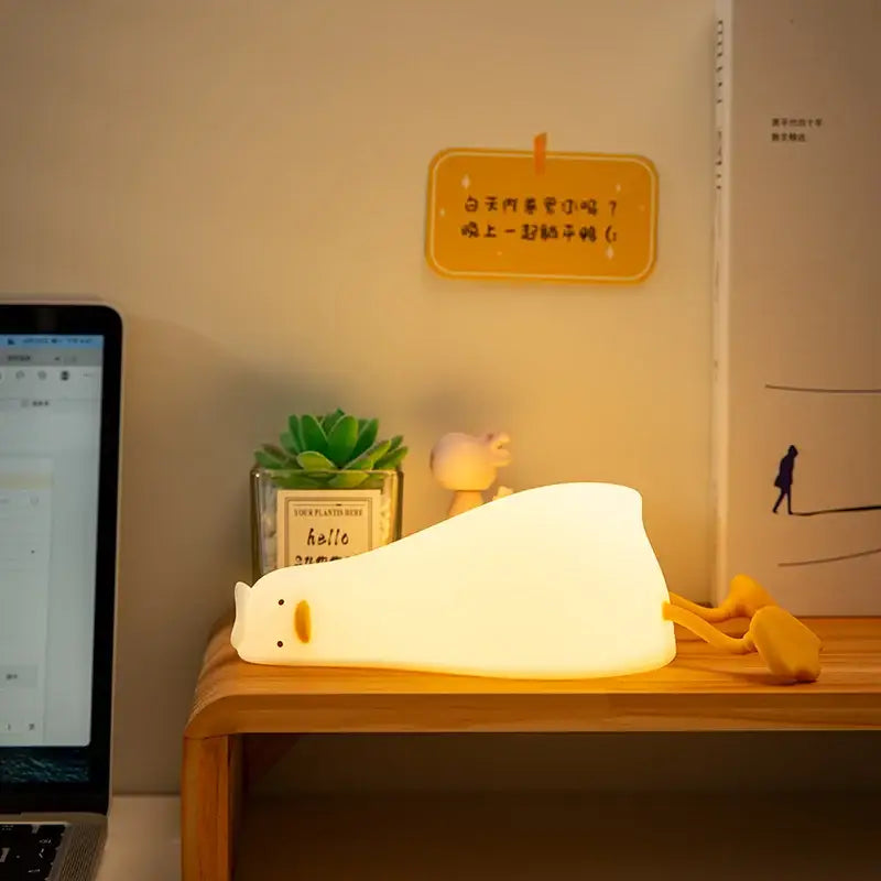 A soft glowing white cat night light with yellow accents paired with decorbites duck silicone night lamp for bedroom use