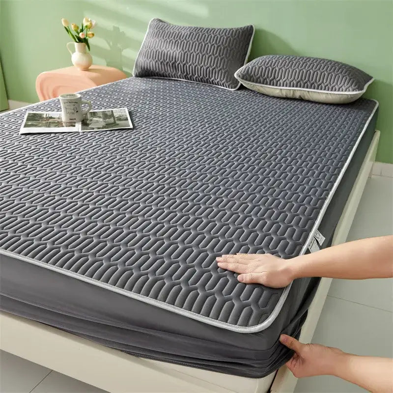 Gray quilted mattress protector with subtle hexagonal pattern and white piping paired with cute cartoon pattern cooling fitted sheet