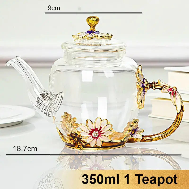 A clear crystal glass teapot set with gold-toned floral embellishments and ornate handle for dining room use