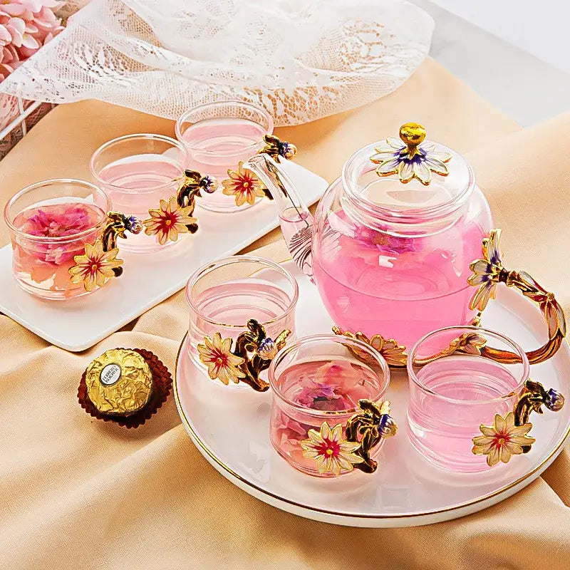 Clear glass teapot set with golden floral handles and lid filled with pink liquid from daisy enamel pink crystal glass set