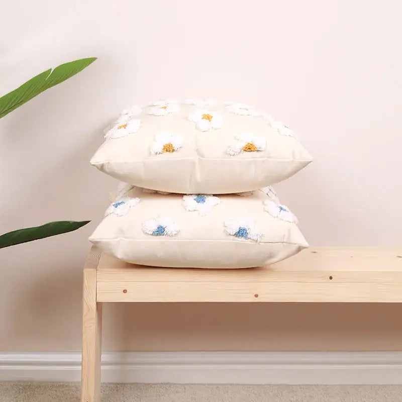 Cream-colored decorbites daisy flora embroidered cushion cover with white daisies and yellow centers on wooden bench