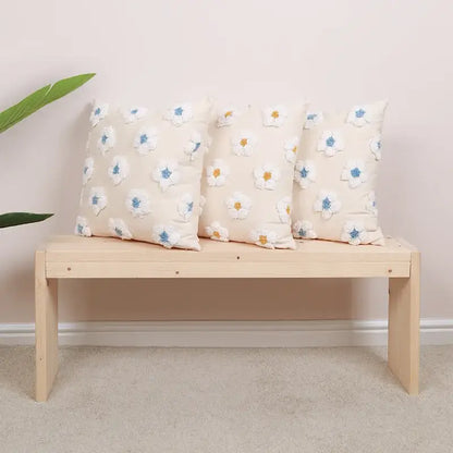 Three cream-colored cushion covers with daisy flora embroidered white flowers on a light wood bench decorbites daisy flora