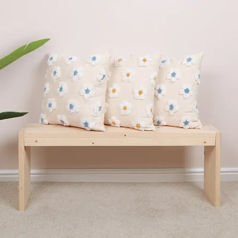 Three cream-colored cushion covers with daisy flora embroidered white flowers on a light wood bench decorbites daisy flora