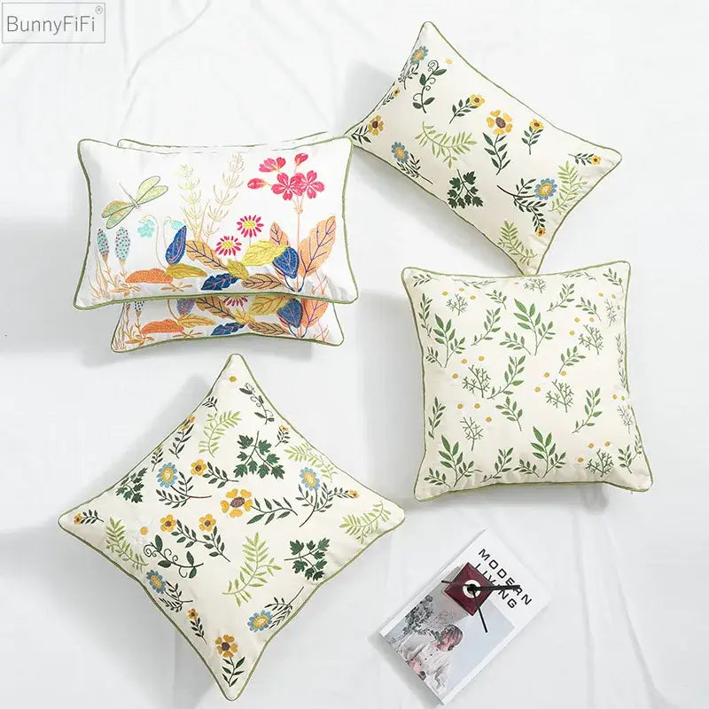 Cream-colored cushion cover with daisy floral embroidery and green leaves accented by olive green piping for decorbites
