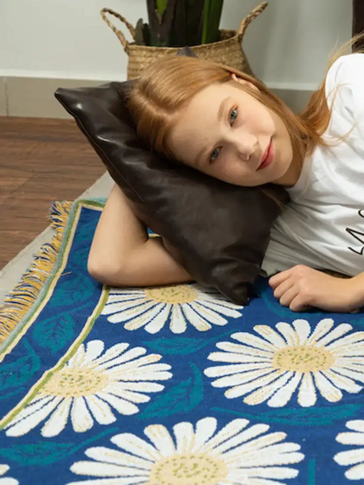 Black leather pillow with smooth glossy finish and soft contours paired with navy and white daisy flower knitted blanket decorbites