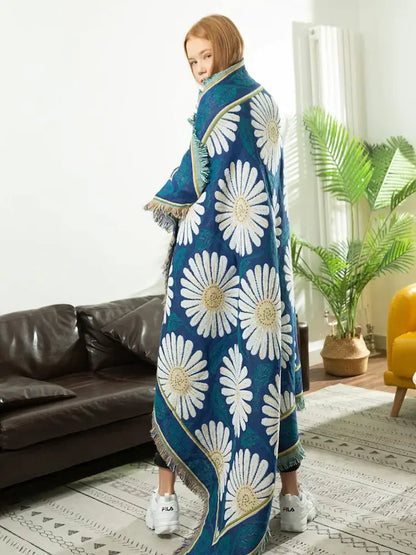 A vibrant blue daisy flower knitted blanket with bold white daisies and gold accents draped over shoulders