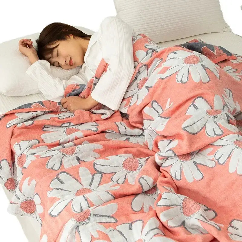 A soft coral-colored double cotton blanket with white daisies draped over a person sleeping in bed