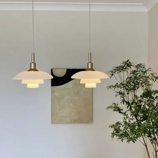 Two elegant Danish tiered frosted glass pendant lights with brass fixtures create a warm focal point for dining rooms