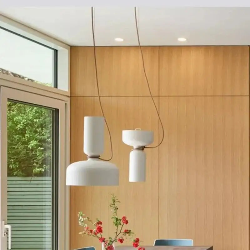 Two minimalist white wrought iron ceramic pendant lights with black cords hanging in a kitchen setting
