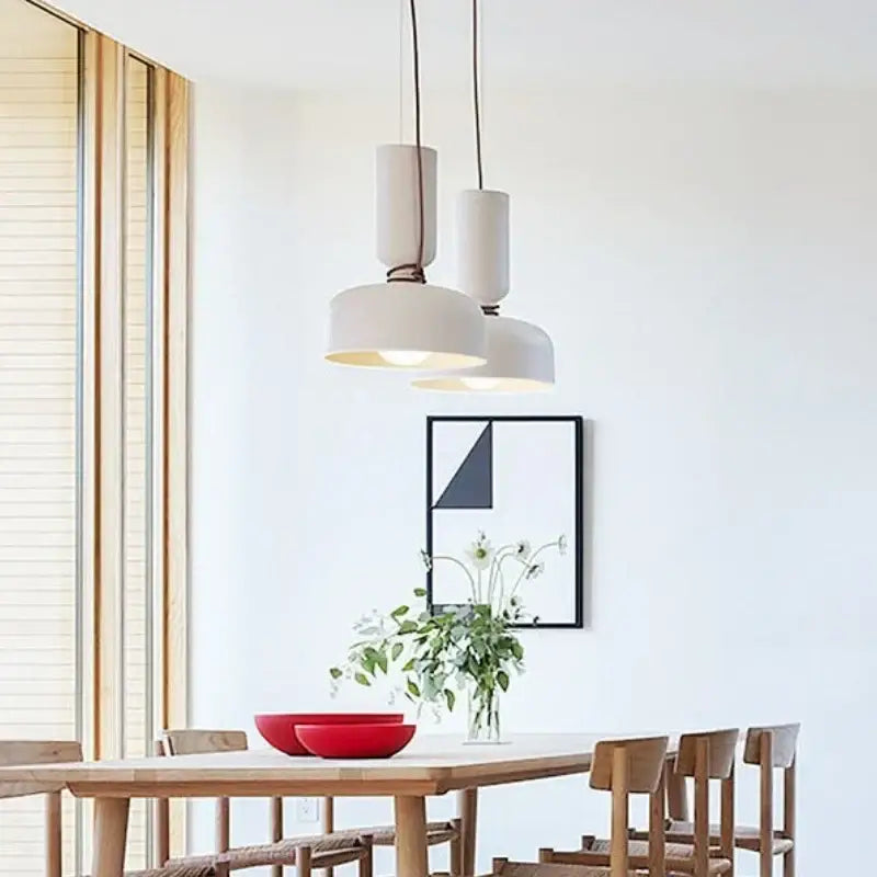 Modern white ceramic pendant light with cylindrical shades and black wrought iron cords above wooden dining table