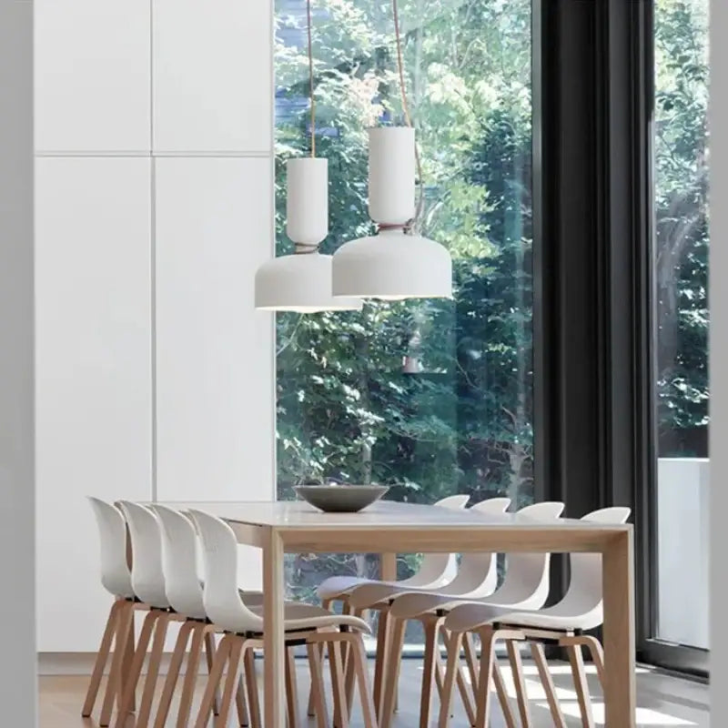 Modern white ceramic pendant light with cylindrical shades and wrought iron cord pendant above wooden dining table