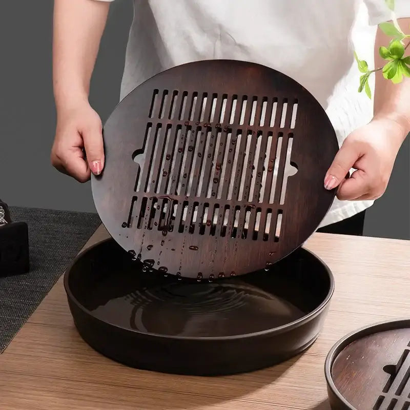Dark brown bamboo tea tray drainage board with vertical slits held above a matching basin for kung fu tea