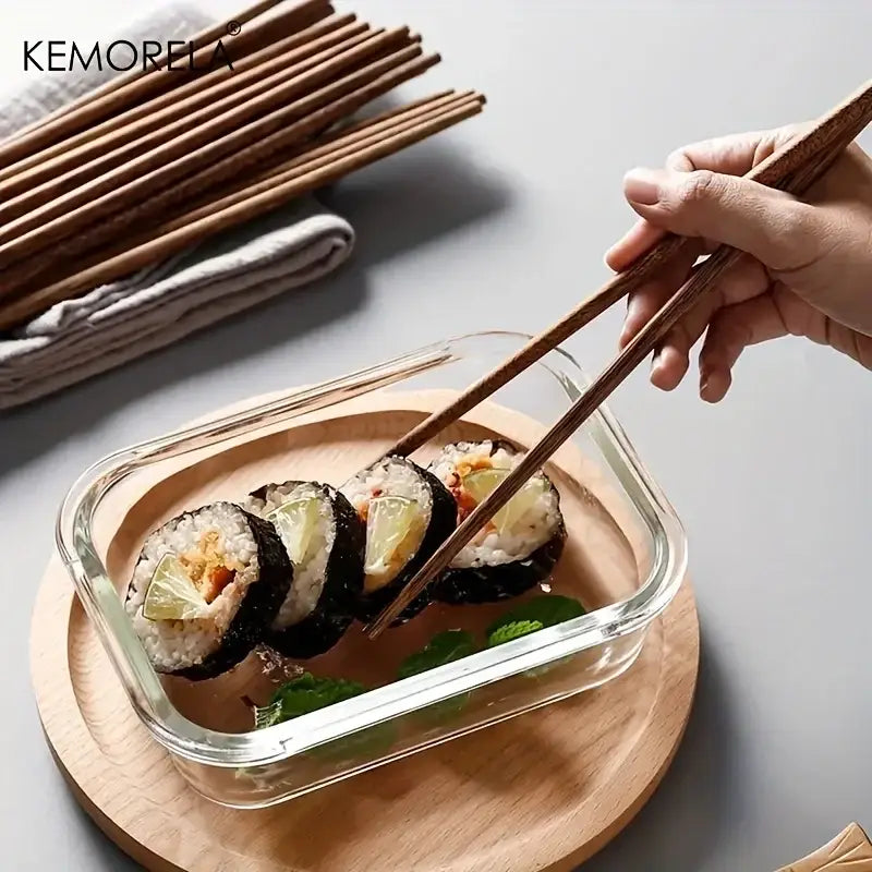 A pair of natural wooden chopsticks picking up sushi from a clear glass container enhancing the dining experience