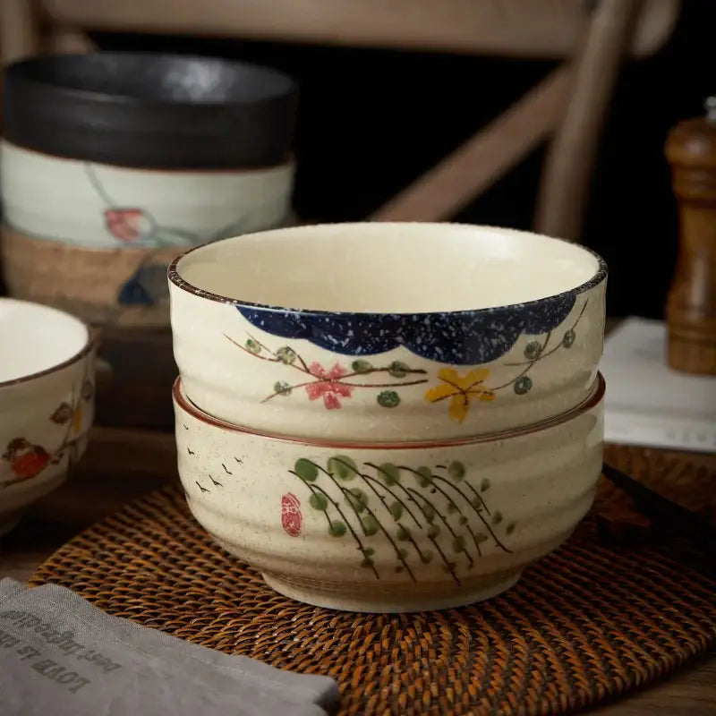 Cream-colored ceramic ramen bowl with navy blue speckled rim and hand-painted floral bird motifs for kitchen use