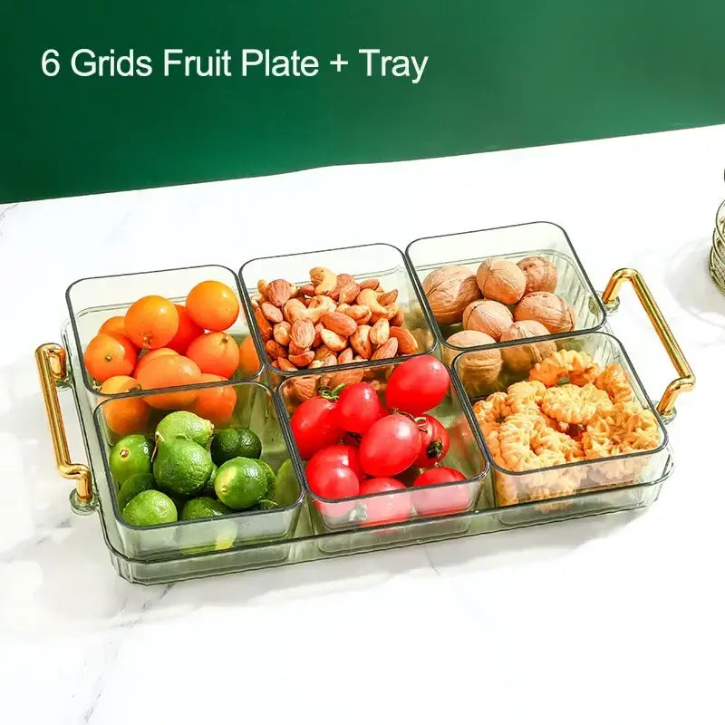 Clear glass 6-grid divided fruit plate with gold-tone handles holding colorful fruits and nuts by DecorBites