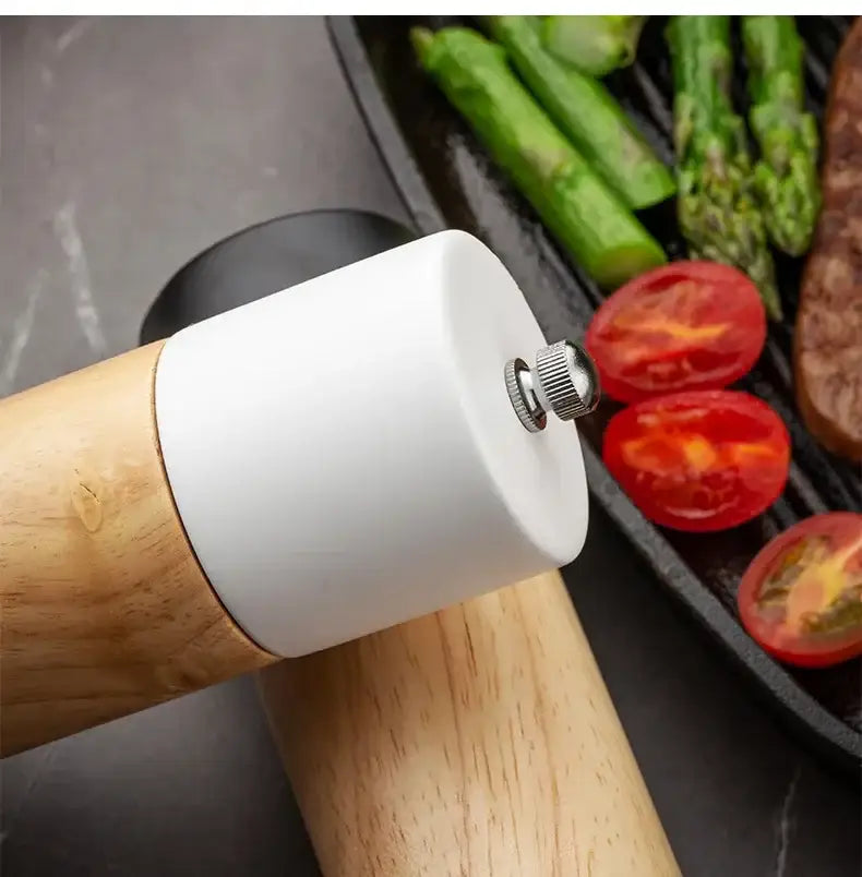 A sleek white ceramic manual wooden salt pepper grinder with natural wood handle resting beside grilled vegetables