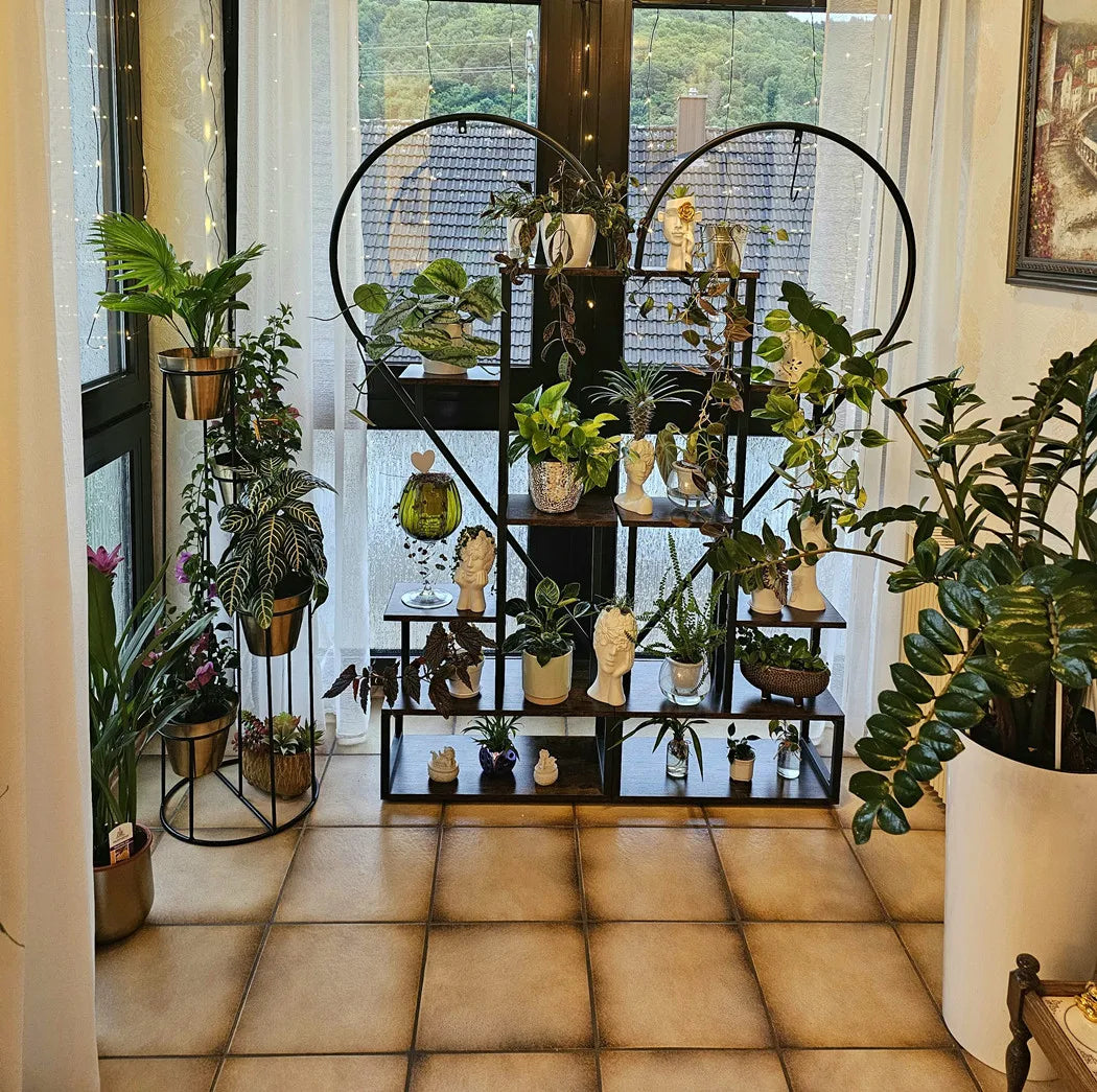 Black metal heart shaped plant display stand with six tiers holding potted plants and decorative figurines by decorbites
