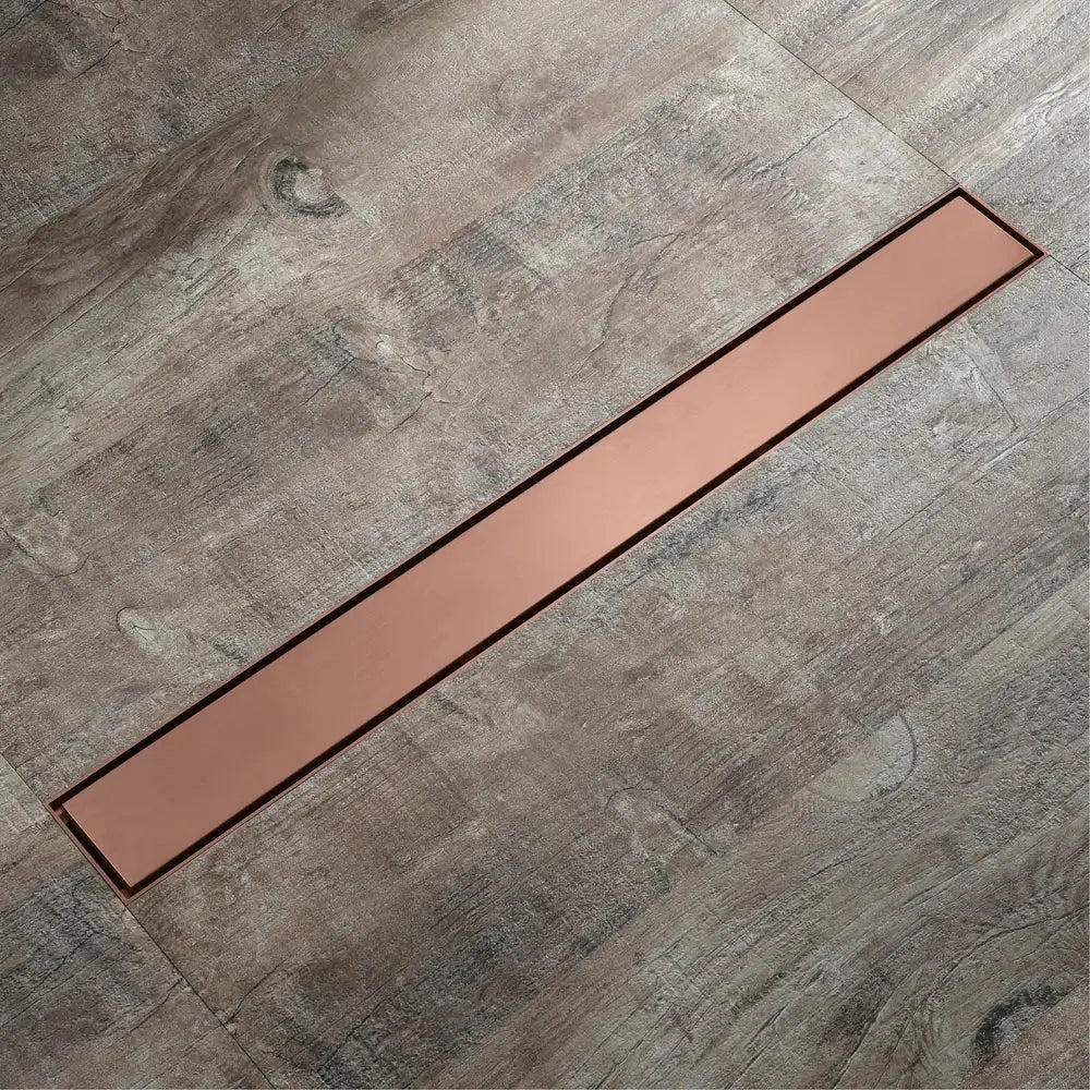 Copper-colored 60cm rose gold bathroom floor drain strainer with sleek modern design set into gray wood-grain flooring