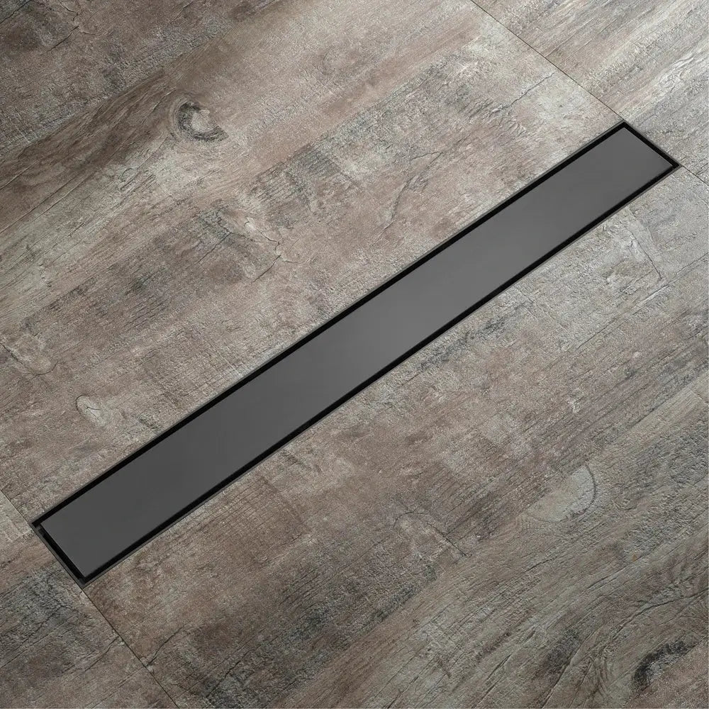 Black rectangular floor drain with sleek modern design embedded in gray wood grain tile for rose gold bathroom use