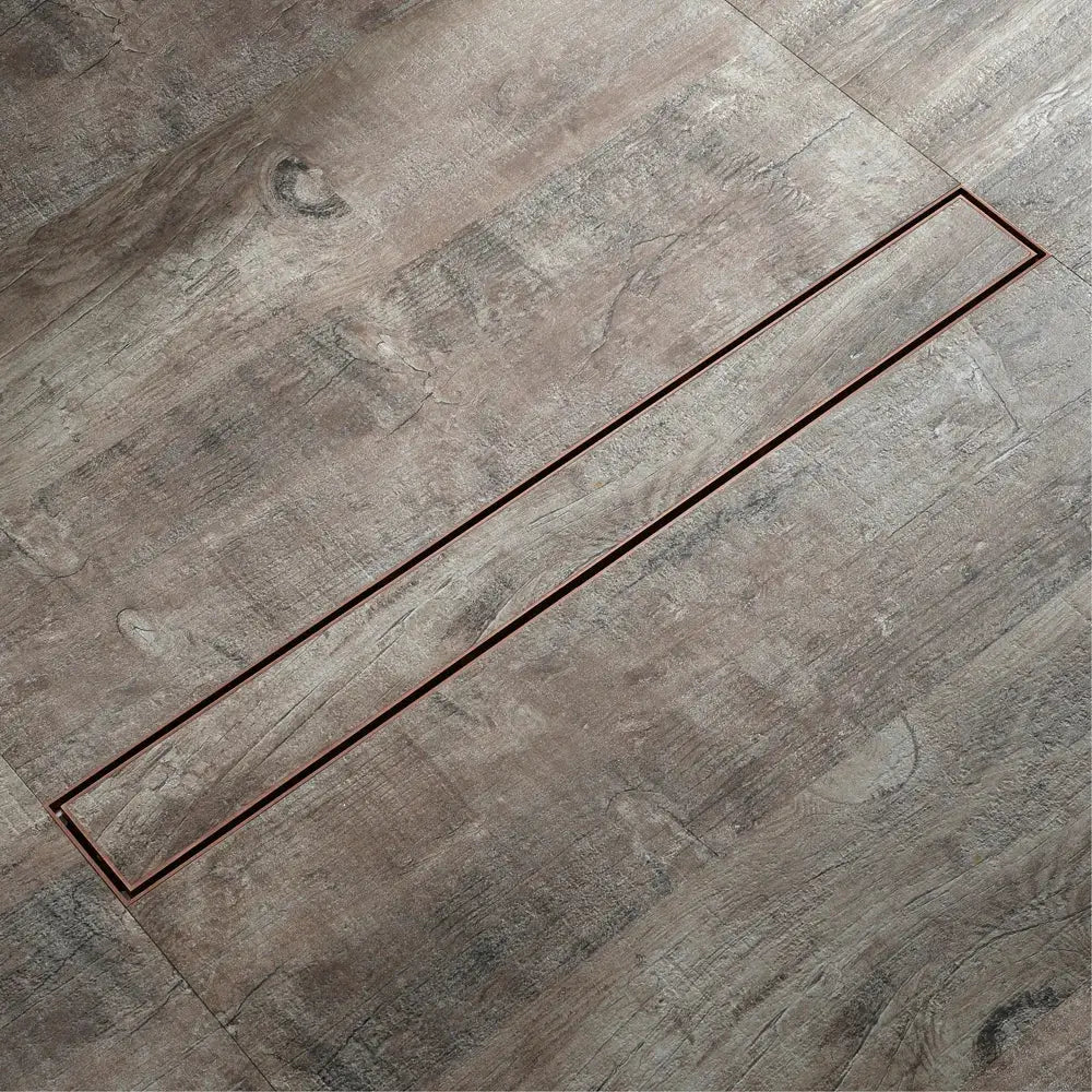 A sleek 60cm rose gold bathroom floor drain strainer with stainless steel design embedded in gray wood flooring