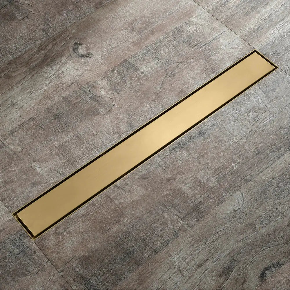A sleek decorbites™ 60cm rose gold bathroom floor drain strainer with polished brass finish on gray wood-look flooring