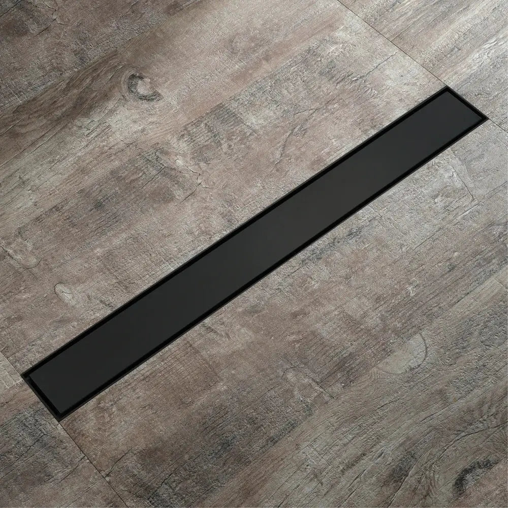 Black rectangular floor drain with sleek modern design set into gray wood-grain tiles for rose gold bathroom use